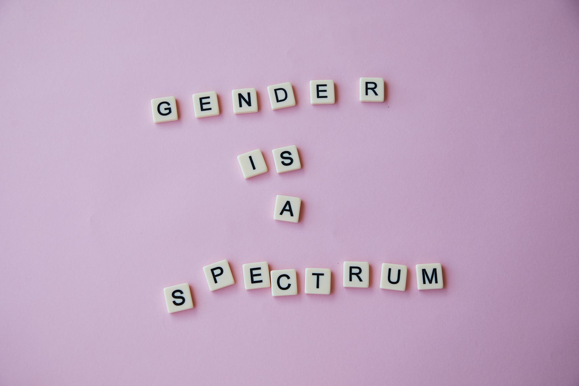 inscription gender is a spectrum made of scrabble letters against pink background